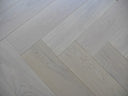White-oiled engineered wood floor showing herringbone plank layout and light gray tone