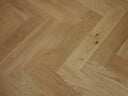 Herringbone wood flooring close-up, light oak-toned planks with small dark knots