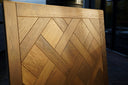 Smoked wood Versailles parquet panel with angled chevron blocks and visible edge