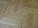 Chevron wood flooring corner detail, light tan planks with oiled sheen