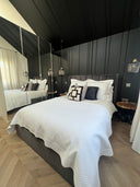 Textured white bed cover with dark geometric pillows on a styled bed