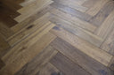 Smoked engineered wood flooring with brushed herringbone pattern, light beige and gray planks