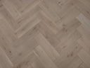 Herringbone wood flooring with pale beige boards and subtle knots across the surface