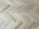 Light gray herringbone engineered wood flooring planks with subtle oil sheen